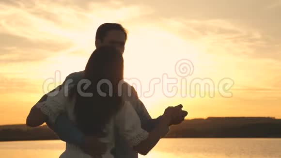 年轻夫妇在海滩上日落时跳舞爱的男人和女人在湖底明亮的阳光下跳舞视频的预览图