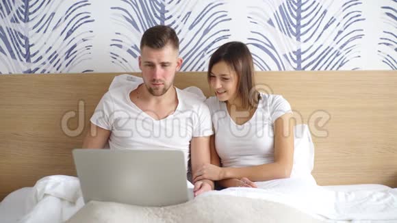年轻夫妇带着笔记本电脑在床上看电影视频的预览图
