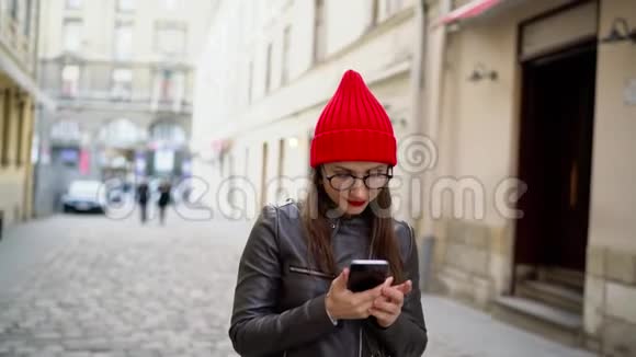 嘴唇红的女人在智能手机上说话沿着中世纪的街道漫步视频的预览图