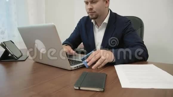年轻的商人正拿着一张信用卡在他的办公室里进行网上购物并在网站上输入信用卡号码视频的预览图