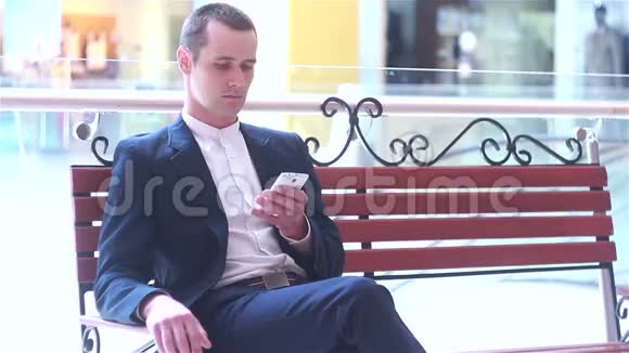 商人正坐在长凳上看着智能手机视频的预览图