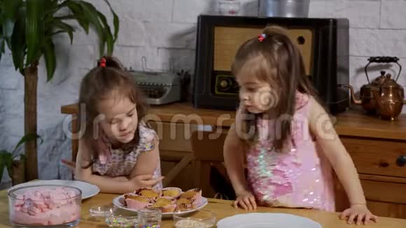 两个小女孩穿上奶油在木桌上装饰美味的纸杯蛋糕视频的预览图
