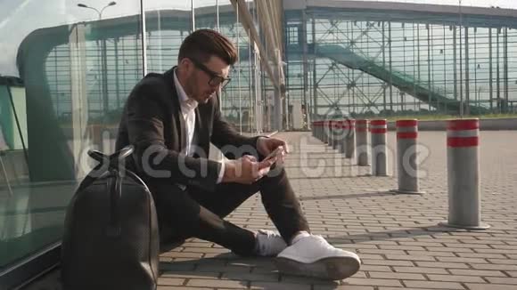 机场车站里长着大胡子的英俊商人在手机上打短信坐在地上视频的预览图