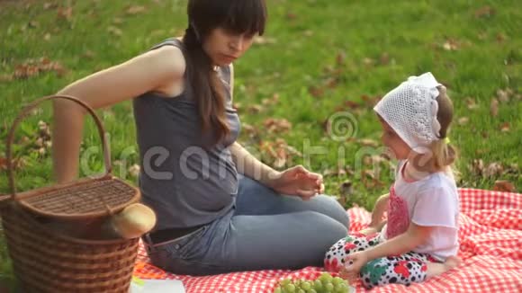 一位快乐的母亲和幸运的女儿在日落时在公共公园野餐视频的预览图