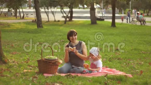 一位快乐的母亲和幸运的女儿在日落时在公共公园野餐视频的预览图