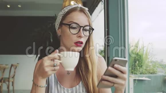 年轻女孩在手机上发短信女人在咖啡馆的智能手机上使用messanger微笑着视频的预览图
