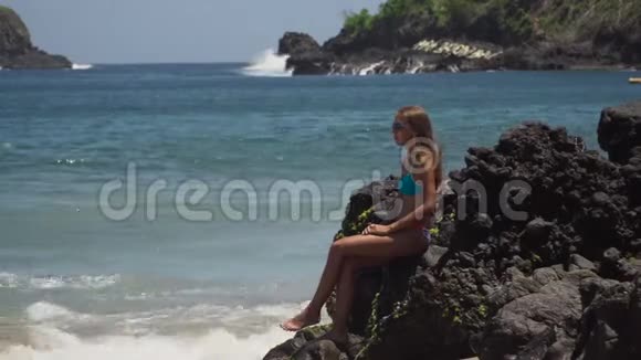 女孩坐在岩石上看着大海印度尼西亚巴厘岛视频的预览图
