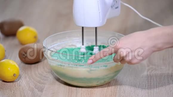 女性用手在碗里搅拌蛋糕用搅拌器搅拌绿色面团视频的预览图