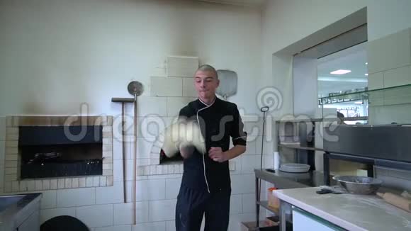 一个年轻的披萨师在餐厅的厨房准备披萨厨师把面团在空气中旋转慢动作视频的预览图