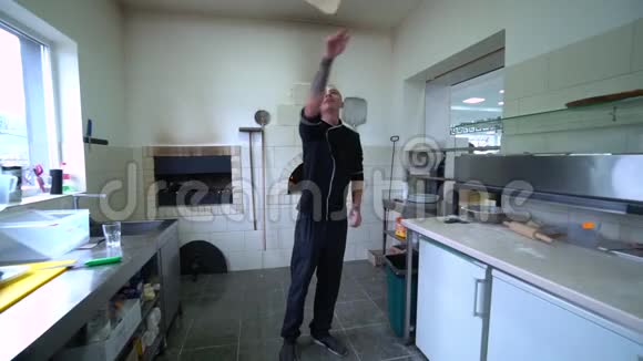 一个年轻的披萨师在餐厅的厨房准备披萨厨师把面团在空气中旋转慢动作视频的预览图