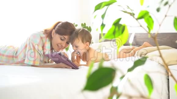 母亲和年幼的儿子在卧室里享受着互联网上的平板电脑视频的预览图