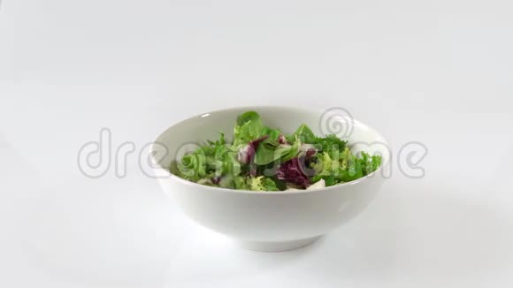 新鲜的绿色沙拉掉进碗里白色隔离的慢动作视频的预览图