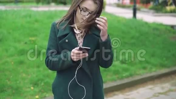 4穿绿色外套的女孩在刮风的日子里听电话里的音乐视频的预览图