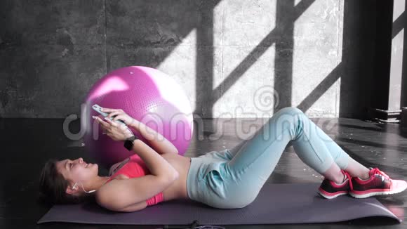 年轻女子运动员坐在垫子上在健身房使用手机20S4K视频的预览图