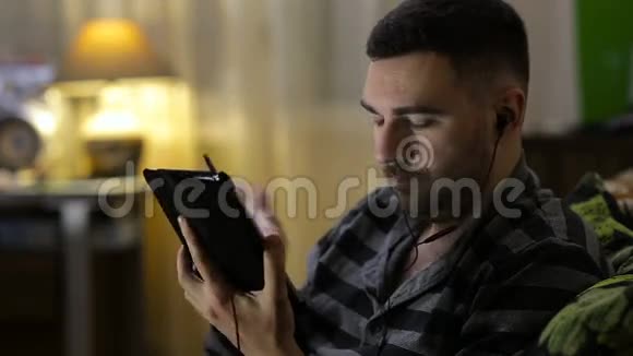 男人在家里用平板电脑看视频或听音乐视频的预览图