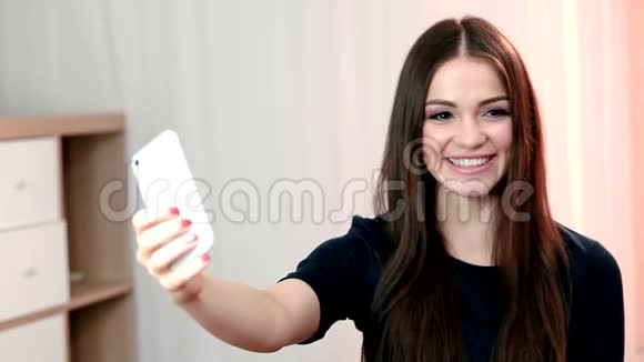 一位美丽成功的微笑女孩在浅色背景下穿着黑色衬衫自拍的肖像视频的预览图
