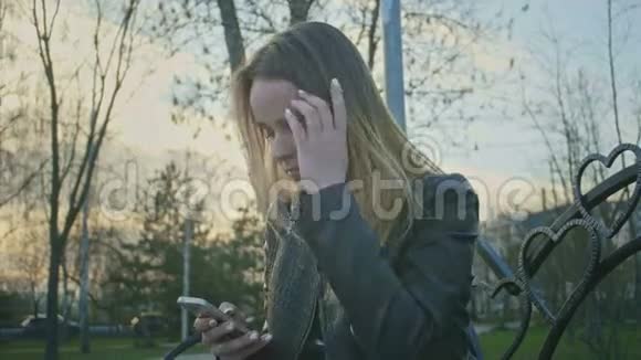 可爱的小女孩使用电话并在日落时将头发伸直坐在长凳上视频的预览图