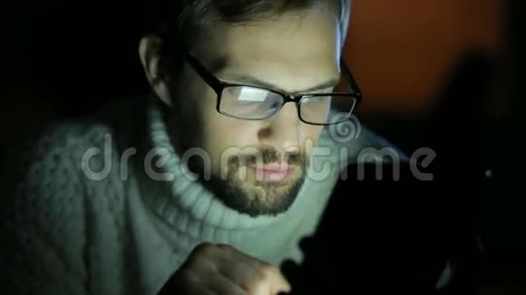 一个戴眼镜穿毛衣在黑暗中拿着平板电脑的家伙视频的预览图