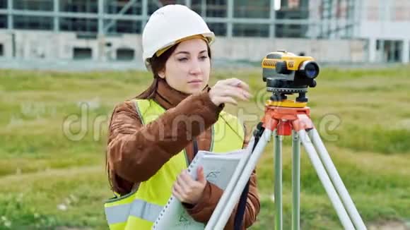 一位穿着工作服和头盔的年轻女性测量员调整设备并对建筑进行计算视频的预览图