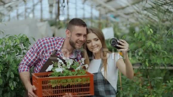 快乐有爱的情侣园丁们在智能手机摄像头上自拍在温室工作时接吻视频的预览图