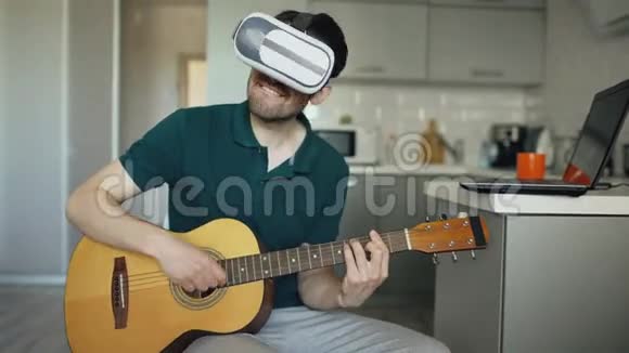 快乐的年轻人坐在厨房里学习用VR360耳机弹吉他并在音乐会上感觉到他是吉他手视频的预览图