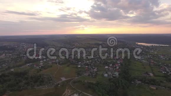 夏季日落时分在河和田野旁的郊区城镇的鸟瞰图视频的预览图
