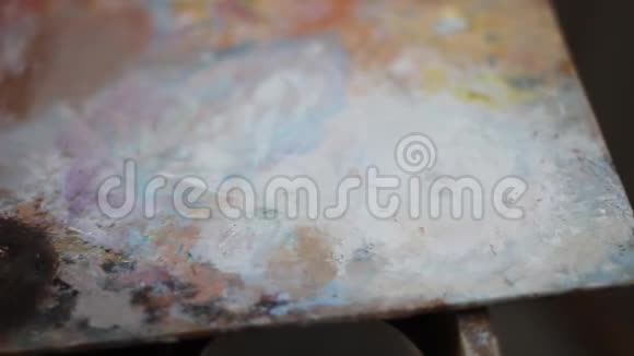 一个年轻人艺术家从一管白色的颜料里挤出来涂在五颜六色的彩色颜料上视频的预览图