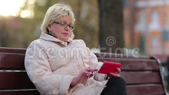 女人坐在路边的长凳上用红色手机视频的预览图