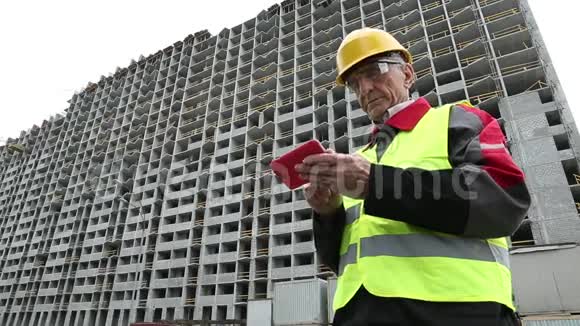 黄色头盔的工程师站在未完工房屋附近的红色智能手机上视频的预览图