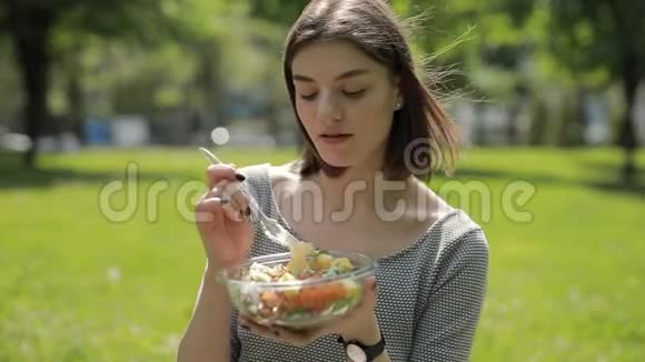 坐在夏日公园里吃新鲜沙拉的女人视频的预览图
