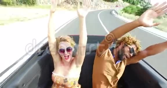 金发女人和黑人男子挥舞着手臂坐在敞篷车的后座上视频的预览图