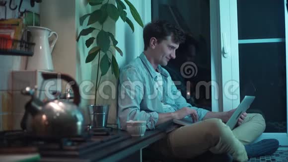年轻人坐在厨房里打电脑一边烧水壶视频的预览图