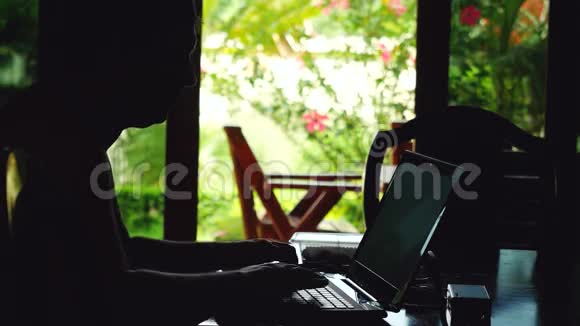 年轻的商人坐在平房里旅行时用笔记本电脑工作视频的预览图
