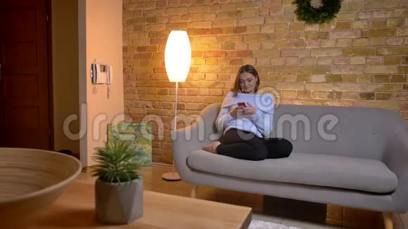 年轻漂亮的白种人女性在室内沙发上打字时的特写镜头视频的预览图