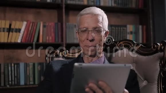 在家图书馆寻找平板电脑信息的老人戴眼镜和现代科技的快乐老人视频的预览图