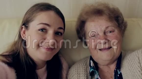 奶奶和年轻女孩在家里坐在沙发或沙发上用手机或智能手机拍照快乐的女士们视频的预览图