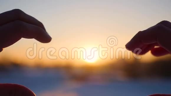 女孩用手在阳光下做心脏剪影手中的心形与里面的夕阳冬季视频的预览图