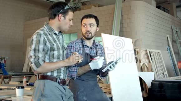 两个木匠讨论工作其中一个在吃饭另一个在车间的笔记本上写视频的预览图