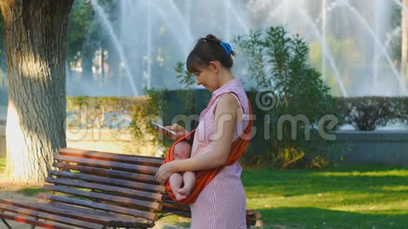 年轻女子带着熟睡的婴儿在吊带快乐的叶子电话画廊视频的预览图