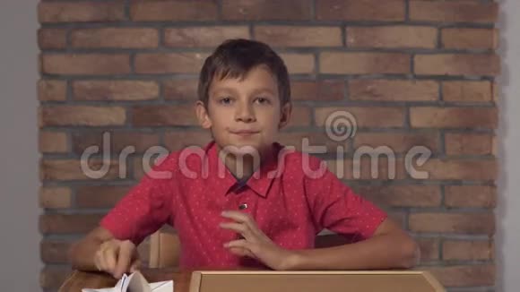坐在书桌前的孩子拿着一张挂图在背景红砖墙上刻着字母视频的预览图