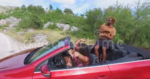 一个英俊的黑人坐在敞篷车的引擎盖上和他的朋友跳舞视频的预览图