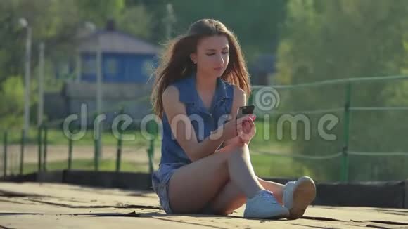 那个女孩拿着一部智能手机智能手机社交媒体上的网络女孩坐在户外铁桥上视频的预览图