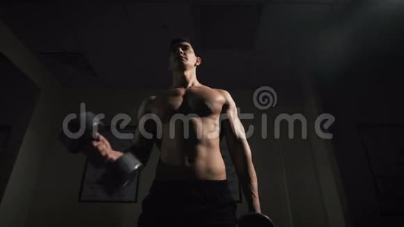 英俊的肌肉男用哑铃在黑暗的背景下工作视频的预览图