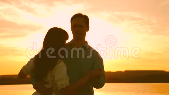 年轻夫妇在海滩上日落时跳舞爱的男人和女人在湖底明亮的阳光下跳舞视频的预览图