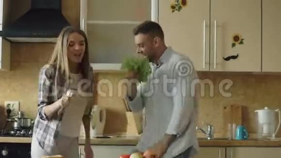 有魅力的年轻快乐的一对夫妇在家厨房做饭的时候玩着跳舞和唱歌的乐趣视频的预览图