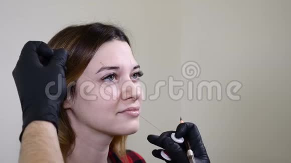 美容院男性美容师戴着黑色手套在永久化妆程序之前涂上眉毛眼线青年视频的预览图