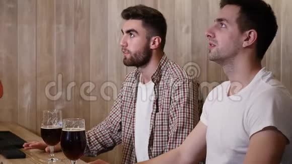两位男性朋友坐沙发看电视上的体育节目视频的预览图