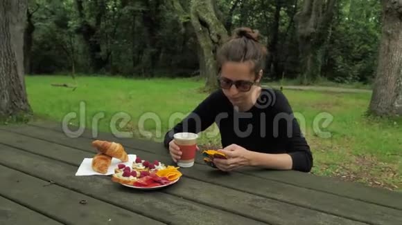 4K漂亮的女孩穿着手工制作的长袖衬衫戴着绿棕色太阳镜坐在木制的乡村餐桌旁视频的预览图