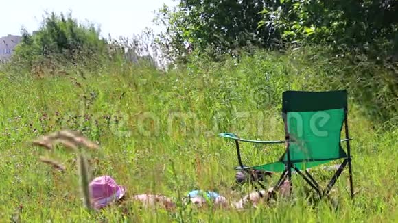 一个穿泳衣的女孩正在草坪上晒日光浴在她旁边的野餐椅上一个男人坐在智能手机里玩视频的预览图