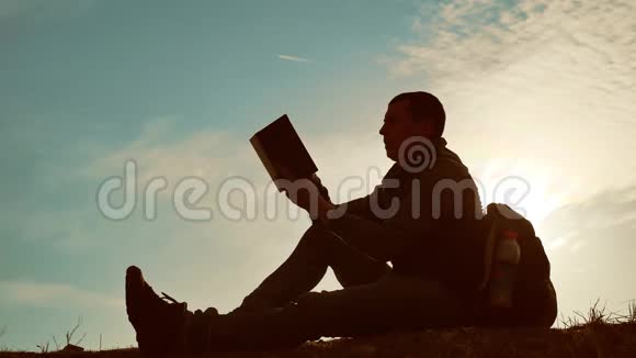 男学生在公园里背着背包看日落生活方式天空夕阳下男子读书剪影视频的预览图